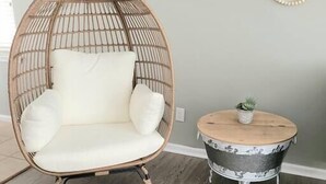 A room with a rattan chair, a round wooden table with a plant, and a round woven ottoman. - Oceanfront Lookout, pet friendly with pool (Carolina Beach)