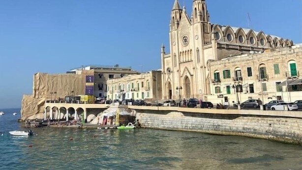 A coastal building with a prominent clock tower, a waterfront promenade, and people relaxing on the beach. - Central APT 5mins to promenade with SOFA AC & WIFI (Sliema)