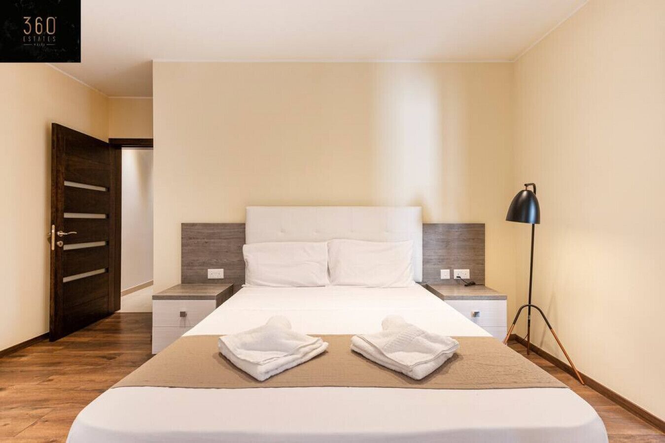 Ein Hotelzimmer mit Bett, Nachttischen, einer Lampe und einer Tür.