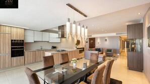 Eine moderne Küche mit einer zentralen Kochinsel, einem Essbereich mit Glastisch und einem Wohnbereich mit Sofa und Fernseher.