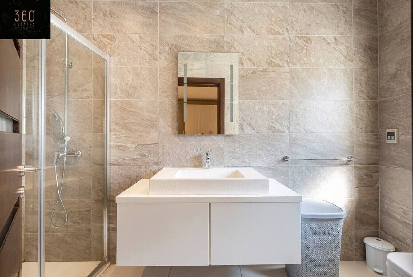 A modern bathroom with a glass-enclosed shower, a white vanity with a mirror, and a marble-tiled wall.