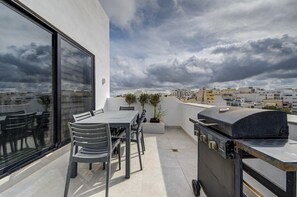 A rooftop terrace with a table and chairs, a grill, and a view of the cityscape. - Penthouse + BBQ Kitchen Island & Massive living (San Ġiljan)