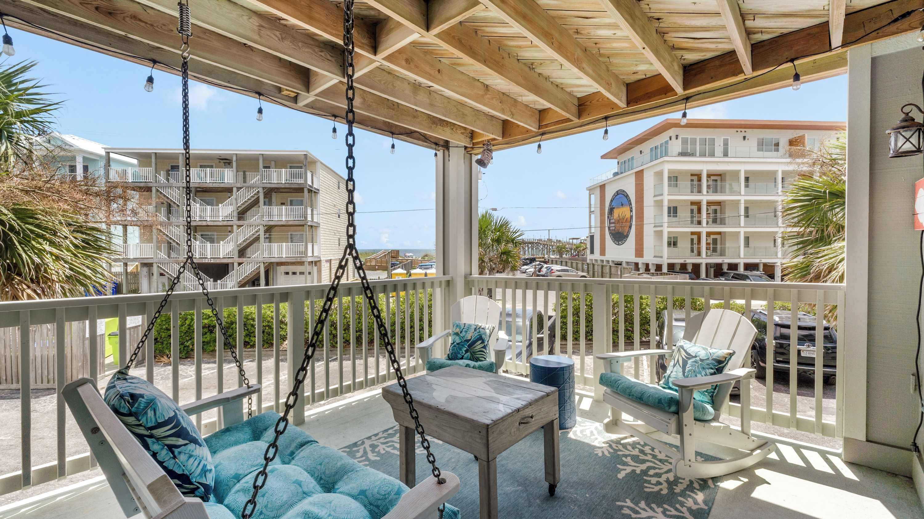 A covered outdoor seating area with a swing chair, a table, and a view of a multi-story building.