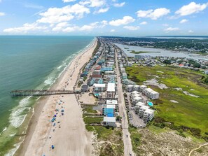 Luchtbeeld van een kustplaats met een lang strand, een pier en een mix van woon- en bedrijfsgebouwen.