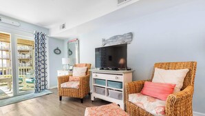 A living room with wicker furniture, a television, and a view of a balcony. - ★ 3 Little Birds at The Beach★ (Carolina Beach)