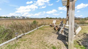 A wooden fence with a metal gate, a chair, and a lamp post in a grassy field with a clear sky. - ★ 3 Little Birds at The Beach★ (Carolina Beach)