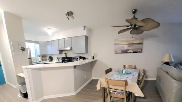 A modern kitchen with white cabinets, a dining area with a table and chairs, and a ceiling fan. - The Narrow Nest @ Sand Pebbles (Carolina Beach)