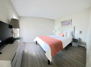 A bedroom with a bed, bedside tables, a desk, and a lamp. - The Narrow Nest @ Sand Pebbles (Carolina Beach)