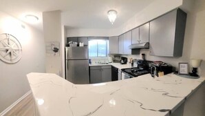 A modern kitchen with a white marble countertop, stainless steel appliances, and grey cabinetry. - The Narrow Nest @ Sand Pebbles (Carolina Beach)