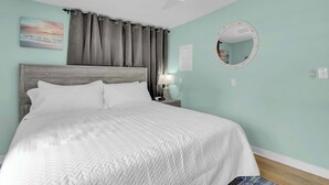 A neatly made bed with a headboard, a bedside lamp, a round mirror, and a wall-mounted picture. - Beachwood Bungalow B, walk to beach and boardwalk (Carolina Beach)