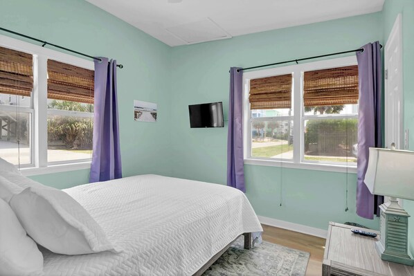A bedroom with a bed, a TV, and a window with curtains.