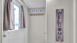 A white door with a window, a 'WELCOME' sign, and three small wall decorations above the door. - Beachwood Bungalow B, walk to beach and boardwalk (Carolina Beach)