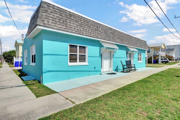 A single-story house with a light blue exterior, a gray shingled roof, and a front porch with two chairs.