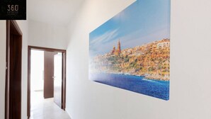 Passadís amb un quadre gran que mostra un paisatge urbà costaner, una porta de fusta i un rètol de '360 Estates'.