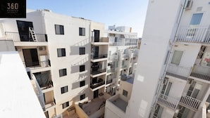 Un edifici residencial de diverses plantes amb balcons, aires condicionadors i un cel serè.