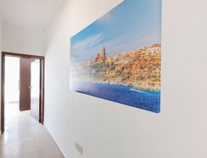 A hallway with a large painting of a coastal cityscape, a wooden door, and a sign for '360 Estates'. - Da Vinci · Spacious central 2BR, just off UNI/Hospital & WIFI (L-Imsida)