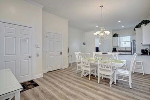 A modern kitchen with white cabinets, a dining area with white chairs, and a chandelier. - Island Treasure, CB Oceanfront Retreat (Carolina Beach)
