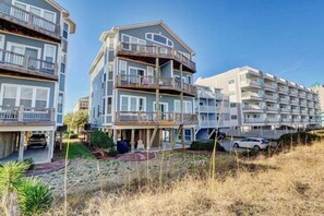 A multi-story residential building with balconies, a driveway, and a landscaped front yard. - Island Treasure, CB Oceanfront Retreat (Carolina Beach)