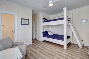 A room with a bunk bed, a desk, a chair, and a ceiling fan. - Island Treasure, CB Oceanfront Retreat (Carolina Beach)