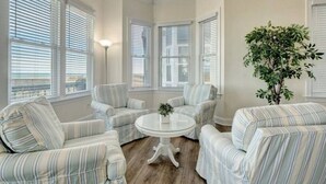 A cozy room with striped upholstered chairs, a round glass table, and large windows with blinds. - Island Treasure, CB Oceanfront Retreat (Carolina Beach)