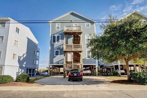 A multi-story residential building with a central balcony, a car parked in front, and a clear sky.