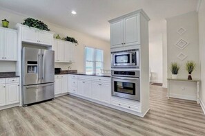 A kitchen with white cabinets, stainless steel appliances, and a wooden floor. - Island Treasure, CB Oceanfront Retreat (Carolina Beach)