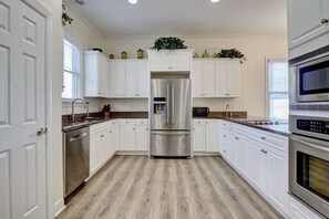 A modern kitchen with white cabinetry, stainless steel appliances, and a wooden floor. - Island Treasure, CB Oceanfront Retreat (Carolina Beach)