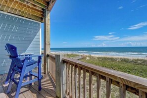 A wooden deck with a view of the ocean, a blue chair, and a table.