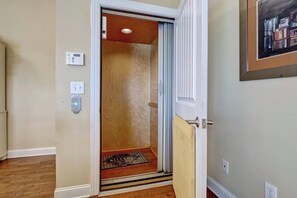 An elevator with a wooden interior, a welcome mat at the bottom, and a wall-mounted thermostat and light switch.