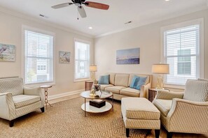 A living room with a beige sofa, patterned armchairs, a coffee table, and a ceiling fan.