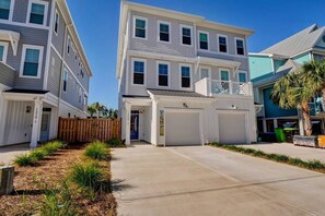 A multi-story residential building with a central garage, a wooden fence, and a landscaped driveway.