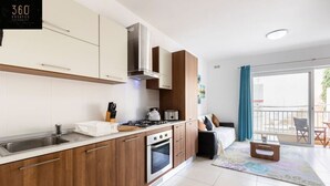 A modern kitchen with wooden cabinets, a stainless steel sink, and a stove. There is a dining area with a table and chairs, and a balcony with a view.