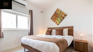 A hotel room with a large bed, a nightstand, a wall-mounted artwork, and a window with curtains.