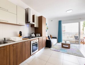 Eine moderne Küche mit Holzausstattung, einer Edelstahlspüle und einem Herd. Es gibt eine Essecke mit Tisch und Stühlen sowie einen Balkon mit Aussicht.