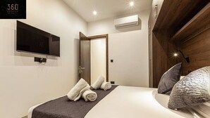 Una habitación de hotel moderna con una cama, un televisor montado en la pared y un equipo de aire acondicionado.