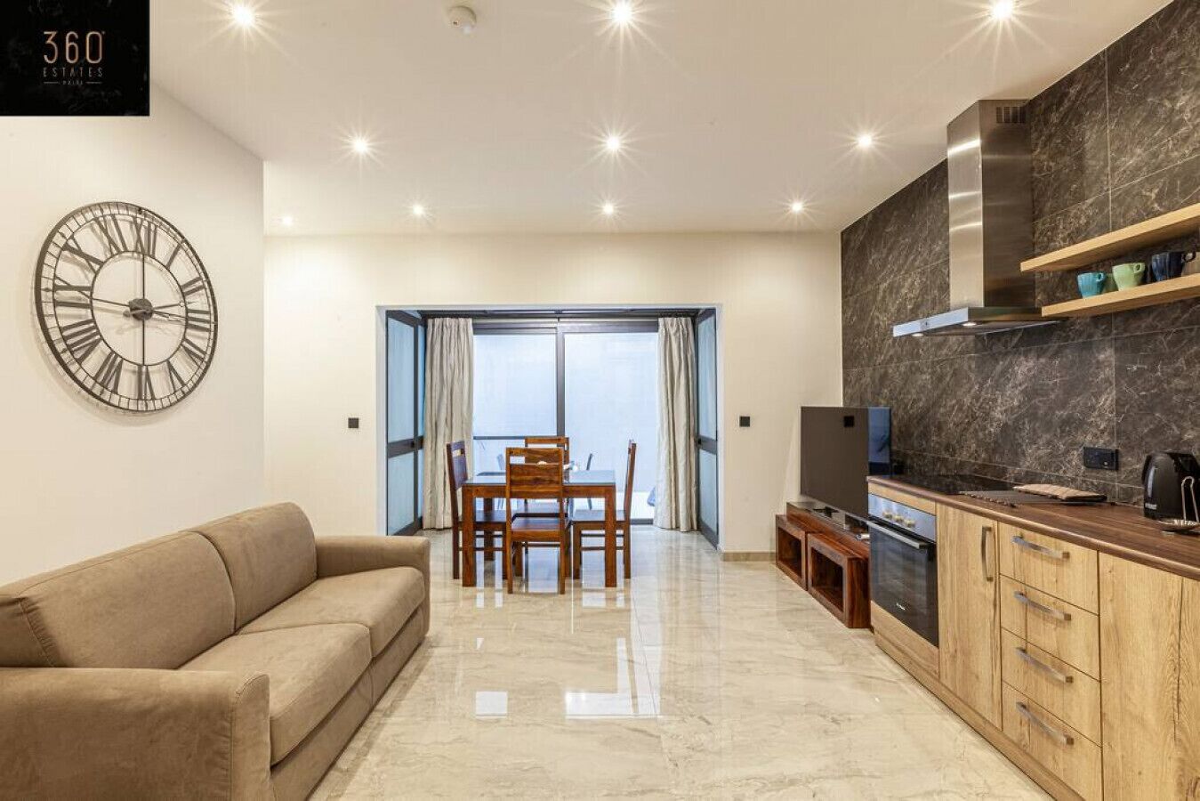 Een moderne woonkamer met een bank, een eettafel met stoelen, een televisie en een keukenhoek met een fornuis en kastjes.