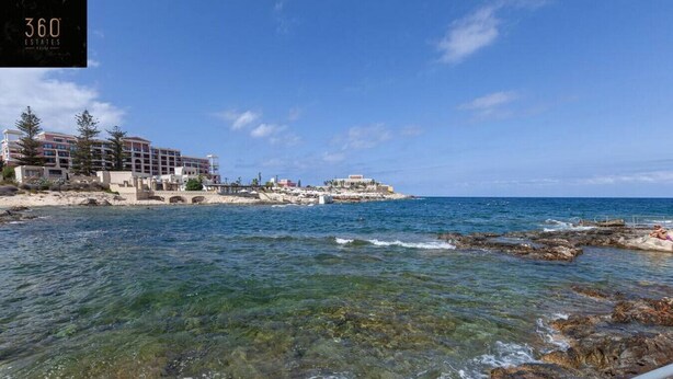 Un hotel frente al mar con aguas cristalinas, costa rocosa y varias construcciones.