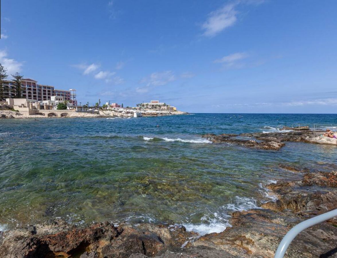 Un hotel frente al mar con aguas cristalinas, costa rocosa y varias construcciones.
