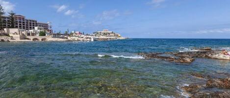 Un hotel frente al mar con aguas cristalinas, costa rocosa y varias construcciones.