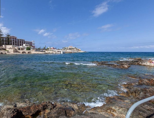 Un hotel frente al mar con aguas cristalinas, costa rocosa y varias construcciones.