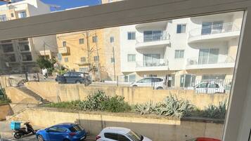 A balcony with a view of a street, a parked scooter, and three cars.