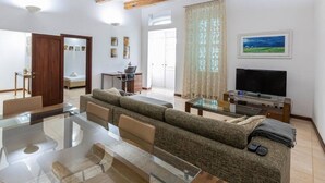 A spacious living room with a glass coffee table, a sofa, a TV, and a wooden ceiling.