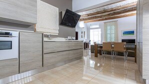 A modern kitchen with a built-in oven, a large island with a sink, and a dining area with chairs.