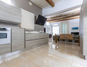 Une cuisine moderne dotée d’un four encastré, d’un grand îlot central avec un évier et d’un coin repas avec des chaises.