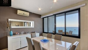 A modern dining area with a large table, chairs, and a view of the sea through large windows. - Sliema Seafront 3BR - opposite Beach - AC & Wifi (Sliema)