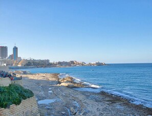 Un paisaje urbano costero con una playa rocosa, un paseo marítimo y una vista despejada del mar.