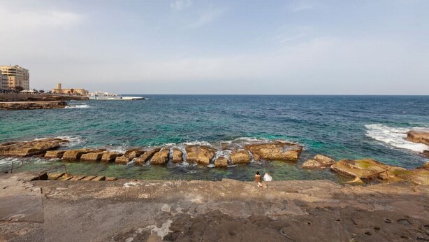 A coastal view with rocky formations and a building in the background. - Spacious Bright Seafront APT (Tas-Sliema)