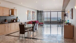 A modern kitchen with marble countertops, a dining area with a glass table, and a view of the sea through large windows. - Spacious Bright Seafront APT (Tas-Sliema)