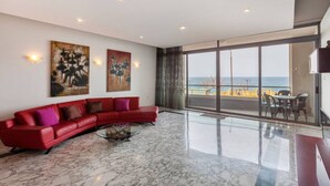 A spacious living room with a red leather sofa, two abstract paintings, and a large glass door leading to a balcony with a view of the sea. - Spacious Bright Seafront APT (Tas-Sliema)