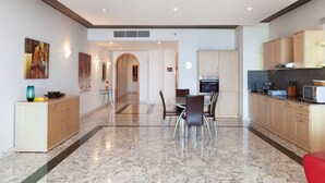 A modern kitchen with marble flooring, wooden cabinets, and a dining area with a glass table and chairs. - Spacious Bright Seafront APT (Tas-Sliema)